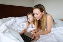 Mujer europea joven que usa el ordenador portátil con la pequeña hija y mintiendo en cama imagenes de archivo Mujer europea joven que usa el ordenador portátil con la pequeña hija y mintiendo en cama imagenes de archivo