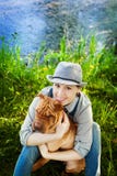 Mujer feliz en guardapolvos y sombrero del dril de algodón con su perro Shar Pei que se sienta en el prado cerca del lago en la p imágenes de archivo libres de regalías Mujer feliz en guardapolvos y sombrero del dril de algodón con su perro Shar Pei que se sienta en el prado cerca del lago en la p imágenes de archivo libres de regalías