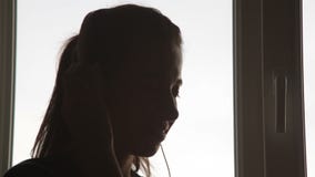 Mujer hermosa en auriculares cerca de la ventana que escucha la música almacen de video Mujer hermosa en auriculares cerca de la ventana que escucha la música almacen de video
