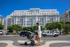 Mujer hermosa joven con el carro de bebé en el fondo del palacio de Copacabana en Rio de Janeiro, el Brasil imagen de archivo libre de regalías Mujer hermosa joven con el carro de bebé en el fondo del palacio de Copacabana en Rio de Janeiro, el Brasil imagen de archivo libre de regalías