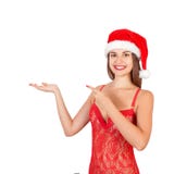 Mujer hermosa joven en sombrero de la Navidad sorprendente y que sonríe a la cámara mientras que presenta con la mano y señala co imagenes de archivo Mujer hermosa joven en sombrero de la Navidad sorprendente y que sonríe a la cámara mientras que presenta con la mano y señala co imagenes de archivo