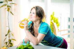 Mujer joven de la aptitud que bebe el smoothie anaranjado en cocina imagen de archivo libre de regalías Mujer joven de la aptitud que bebe el smoothie anaranjado en cocina imagen de archivo libre de regalías