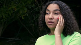 Mujer joven del adolescente afroamericano biracial hermoso de la muchacha que habla en una llamada de teléfono en su teléfono cel almacen de metraje de vídeo Mujer joven del adolescente afroamericano biracial hermoso de la muchacha que habla en una llamada de teléfono en su teléfono cel almacen de metraje de vídeo