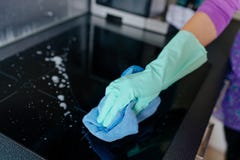 Mujer joven en los guantes de goma que limpian la cocina de inducción moderna fotografía de archivo libre de regalías Mujer joven en los guantes de goma que limpian la cocina de inducción moderna fotografía de archivo libre de regalías