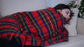 Mujer joven hermosa que miente en el sofá debajo de la manta en casa y que sonríe en la cámara almacen de video Mujer joven hermosa que miente en el sofá debajo de la manta en casa y que sonríe en la cámara almacen de video