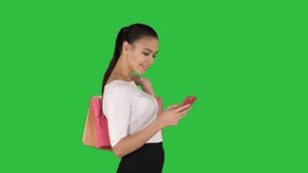 Mujer joven hermosa usando un tel?fono m?vil que camina y que sostiene bolsos de compras en una pantalla verde, llave de la croma almacen de video Mujer joven hermosa usando un tel?fono m?vil que camina y que sostiene bolsos de compras en una pantalla verde, llave de la croma almacen de video
