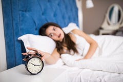 Mujer joven soñolienta de la belleza que estira la mano a la alarma de sonido para apagarla Despierte temprano, no consiguiendo b foto de archivo Mujer joven soñolienta de la belleza que estira la mano a la alarma de sonido para apagarla Despierte temprano, no consiguiendo b foto de archivo