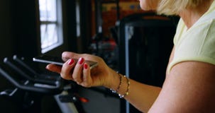 Mujer mayor que habla en el teléfono móvil durante ejercicio en el estudio 4k de la aptitud almacen de metraje de vídeo Mujer mayor que habla en el teléfono móvil durante ejercicio en el estudio 4k de la aptitud almacen de metraje de vídeo
