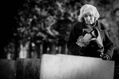 Mujer mayor triste con las flores que hacen una pausa el sepulcro imagen de archivo Mujer mayor triste con las flores que hacen una pausa el sepulcro imagen de archivo