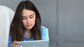 Mujer morena que miente en el sofá y que usa la tableta en casa en la sala de estar almacen de video Mujer morena que miente en el sofá y que usa la tableta en casa en la sala de estar almacen de video