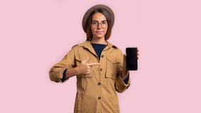 Mujer morena que señala a la pantalla negra del smartphone, aislada sobre fondo rosado fotografía de archivo libre de regalías Mujer morena que señala a la pantalla negra del smartphone, aislada sobre fondo rosado fotografía de archivo libre de regalías