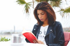 Mujer preciosa joven que se sienta en el libro interesante de la lectura pensativa de la terraza de la cafetería fotografía de archivo libre de regalías Mujer preciosa joven que se sienta en el libro interesante de la lectura pensativa de la terraza de la cafetería fotografía de archivo libre de regalías