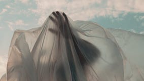 Mujer que alcanza hacia fuera con su mano debajo de hoja plástica Mujer que alcanza hacia fuera con su mano debajo de hoja plástica