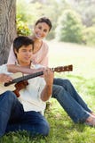 Mujer que detiene a su amigo como sus juegos la guitarra fotos de archivo Mujer que detiene a su amigo como sus juegos la guitarra fotos de archivo
