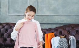 Mujer que se sienta en el sofá ella está sosteniendo una camisa rosada y está sonriendo imagen de archivo libre de regalías Mujer que se sienta en el sofá ella está sosteniendo una camisa rosada y está sonriendo imagen de archivo libre de regalías