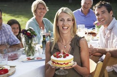 Mujer que sostiene la torta de cumpleaños con la familia en jardín foto de archivo Mujer que sostiene la torta de cumpleaños con la familia en jardín foto de archivo