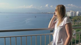 Mujer que tiene charla del teléfono y que disfruta de la opinión del mar del balcón metrajes Mujer que tiene charla del teléfono y que disfruta de la opinión del mar del balcón metrajes