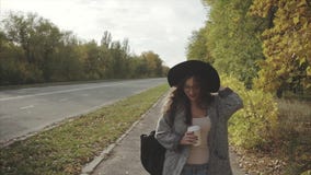 Mujer sonriente bonita joven en sombrero negro que camina abajo de la calle del otoño almacen de video Mujer sonriente bonita joven en sombrero negro que camina abajo de la calle del otoño almacen de video