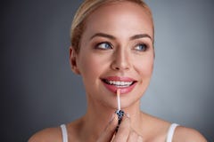 Mujer sonriente que aplica labio-lustre en los labios Fotografía de archivo Mujer sonriente que aplica labio-lustre en los labios Fotografía de archivo