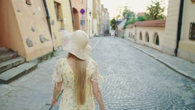 Mujer sonriente que camina en la calle Mujer bonita alegre en el sombrero blanco que mira detrás la cámara mientras que camina en almacen de video Mujer sonriente que camina en la calle Mujer bonita alegre en el sombrero blanco que mira detrás la cámara mientras que camina en almacen de video