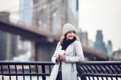 Mujer turística adulta sonriente feliz que sostiene la taza de café de papel y que disfruta de la opinión de New York City imagen de archivo Mujer turística adulta sonriente feliz que sostiene la taza de café de papel y que disfruta de la opinión de New York City imagen de archivo