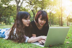 Mujeres asiáticas jovenes del inconformista feliz que trabajan en el ordenador portátil en parque El estudiar en la hierba fotos de archivo Mujeres asiáticas jovenes del inconformista feliz que trabajan en el ordenador portátil en parque El estudiar en la hierba fotos de archivo