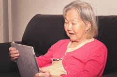 Mulher adulta assentada em um sofá usando uma tabuleta do écran sensível imagem de stock Mulher adulta assentada em um sofá usando uma tabuleta do écran sensível imagem de stock