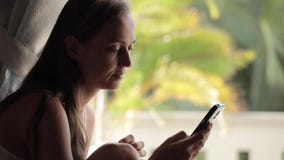 Mulher atrativa nova que usa o telefone esperto em casa perto da janela vídeos de arquivo Mulher atrativa nova que usa o telefone esperto em casa perto da janela vídeos de arquivo
