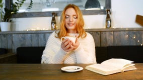 A mulher bonita nova está lendo um livro no café É de sorriso e de apreciação o aroma do café filme A mulher bonita nova está lendo um livro no café É de sorriso e de apreciação o aroma do café filme