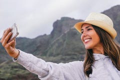 Mulher bonita nova nas f?rias que tomam um selfie com sua c?mera m?vel do smartphone com a montanha no fundo foto de stock Mulher bonita nova nas f?rias que tomam um selfie com sua c?mera m?vel do smartphone com a montanha no fundo foto de stock