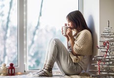 Mulher bonita nova que bebe o café quente que senta-se no peitoril da janela Imagens de Stock Mulher bonita nova que bebe o café quente que senta-se no peitoril da janela Imagens de Stock