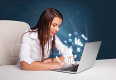 Mulher bonita que senta-se na mesa e que datilografa no portátil com diagramas Fotografia de Stock Royalty Free Mulher bonita que senta-se na mesa e que datilografa no portátil com diagramas Fotografia de Stock Royalty Free