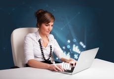 Mulher bonita que senta-se na mesa e que datilografa no portátil com diagramas Fotografia de Stock Mulher bonita que senta-se na mesa e que datilografa no portátil com diagramas Fotografia de Stock