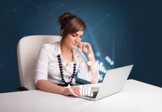 Mulher bonita que senta-se na mesa e que datilografa no portátil com diagramas Fotos de Stock Mulher bonita que senta-se na mesa e que datilografa no portátil com diagramas Fotos de Stock