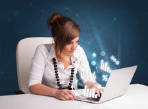 Mulher bonita que senta-se na mesa e que datilografa no portátil com diagramas Imagens de Stock Mulher bonita que senta-se na mesa e que datilografa no portátil com diagramas Imagens de Stock