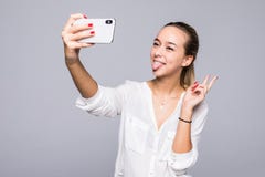 Mulher bonita que toma o selfie e que mostra o sinal da vitória com sorriso perfeito isolado sobre o fundo cinzento fotos de stock Mulher bonita que toma o selfie e que mostra o sinal da vitória com sorriso perfeito isolado sobre o fundo cinzento fotos de stock