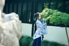 Mulher chinesa asiática no vestido azul e branco tradicional de Hanfu, jogo em um jardim famoso perto das janelas foto de stock royalty free Mulher chinesa asiática no vestido azul e branco tradicional de Hanfu, jogo em um jardim famoso perto das janelas foto de stock royalty free