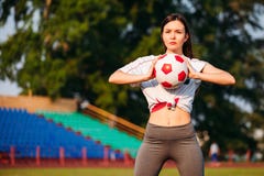 Mulher com a bola de futebol em suas mãos no campo de futebol no fundo dos suportes foto de stock Mulher com a bola de futebol em suas mãos no campo de futebol no fundo dos suportes foto de stock
