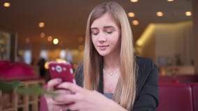 A mulher com o cabelo louro bonito no revestimento preto está sentando-se na loja do café Texting com ela filme A mulher com o cabelo louro bonito no revestimento preto está sentando-se na loja do café Texting com ela filme