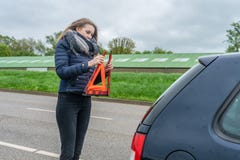 A mulher com uma divisão do carro montou o triângulo de advertência atrás de seu carro imagens de stock A mulher com uma divisão do carro montou o triângulo de advertência atrás de seu carro imagens de stock