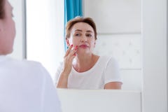 Mulher da Idade Média que olha no espelho na cara com os malotes sob os olhos Enrugamentos, conceito antienvelhecimento dos cuida imagem de stock Mulher da Idade Média que olha no espelho na cara com os malotes sob os olhos Enrugamentos, conceito antienvelhecimento dos cuida imagem de stock