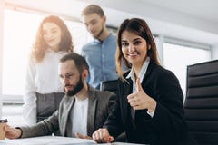 Mulher de negócios atrativa que sorri na câmera e que mostra o polegar acima durante uma reunião de negócios imagem de stock Mulher de negócios atrativa que sorri na câmera e que mostra o polegar acima durante uma reunião de negócios imagem de stock