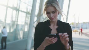A mulher de negócios lindo com penteado formal passa com pressa o terminal de aeroporto, texts a mensagem em seu telefone vídeos de arquivo A mulher de negócios lindo com penteado formal passa com pressa o terminal de aeroporto, texts a mensagem em seu telefone vídeos de arquivo