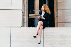 Mulher de negócios magro com cabelo luxuoso ondulado, tendo os pés delgados, terno elegante preto vestindo e sapatas, guardando o fotos de stock royalty free Mulher de negócios magro com cabelo luxuoso ondulado, tendo os pés delgados, terno elegante preto vestindo e sapatas, guardando o fotos de stock royalty free
