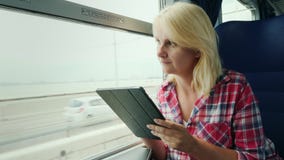 A mulher está viajando em um trem Senta-se pela janela, usa-se uma tabuleta digital video estoque A mulher está viajando em um trem Senta-se pela janela, usa-se uma tabuleta digital video estoque