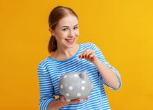 Mulher feliz com o banco leit?o do dinheiro no fundo amarelo Conceito do planeamento financeiro imagem de stock royalty free Mulher feliz com o banco leit?o do dinheiro no fundo amarelo Conceito do planeamento financeiro imagem de stock royalty free