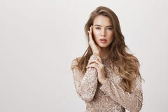Mulher feminino atrativa com o cabelo longo bonito que está no vestido de noite elegante, tocando levemente na cara como se sobre imagens de stock royalty free Mulher feminino atrativa com o cabelo longo bonito que está no vestido de noite elegante, tocando levemente na cara como se sobre imagens de stock royalty free