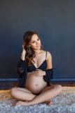 Mulher gravida feliz bonita que senta-se em seu roupa interior no assoalho foto de stock Mulher gravida feliz bonita que senta-se em seu roupa interior no assoalho foto de stock