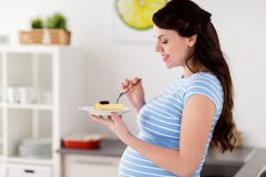 Mulher gravida feliz que come a cozinha do bolo em casa fotografia de stock Mulher gravida feliz que come a cozinha do bolo em casa fotografia de stock