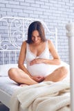 Mulher gravida feliz que guarda a barriga na cama imagem de stock royalty free Mulher gravida feliz que guarda a barriga na cama imagem de stock royalty free